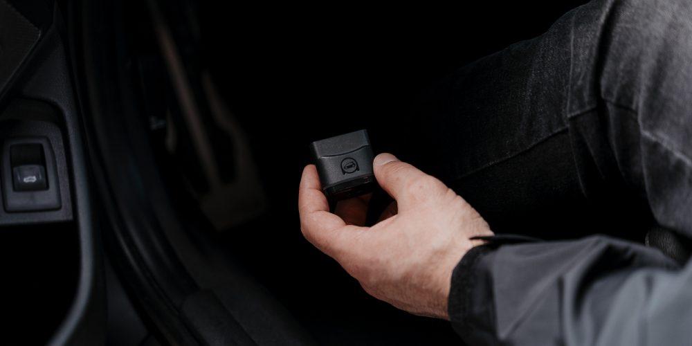 A person inside a car is holding an OBDeleven device and is ready to plug it in OBD2 port.