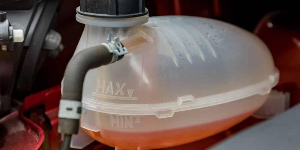 An engine coolant reservoir with visible 'MAX' and 'MIN' level markings, containing coolant fluid below 'MIN' level.