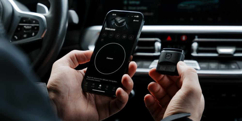 A person inside a car is holding an OBDeleven app and device.