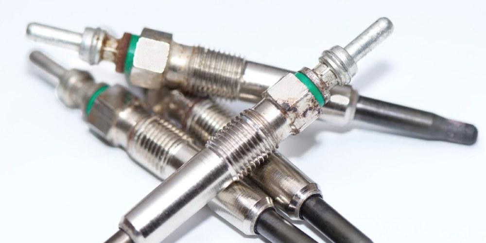 A close-up photo of several used glow plugs laid out on a white surface