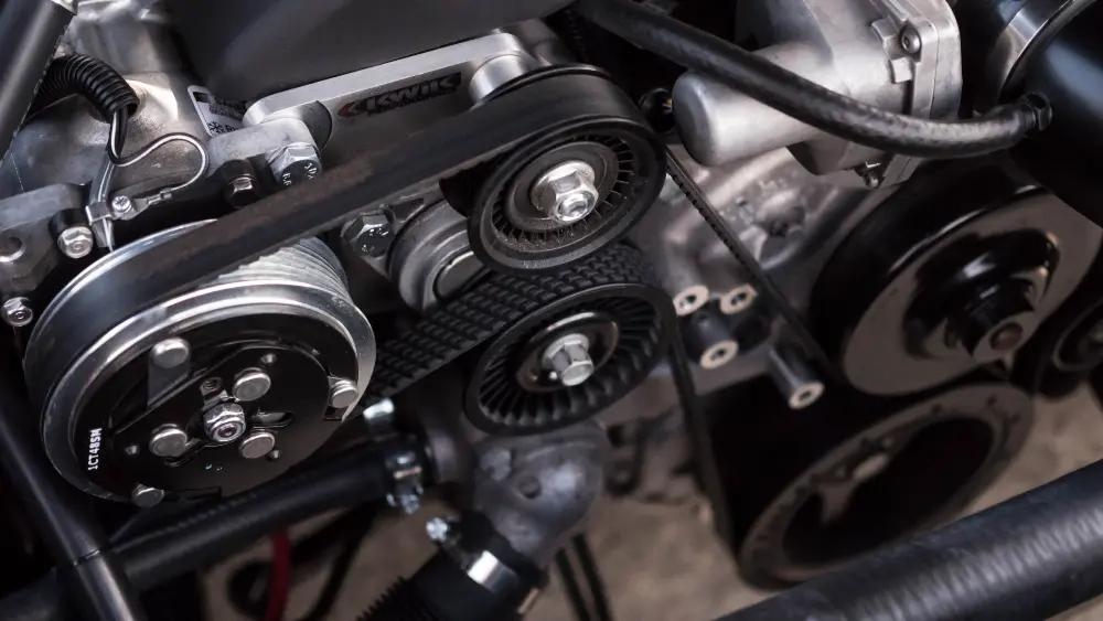 Close-up of an engine serpentine belt and pulley system in a vehicle.