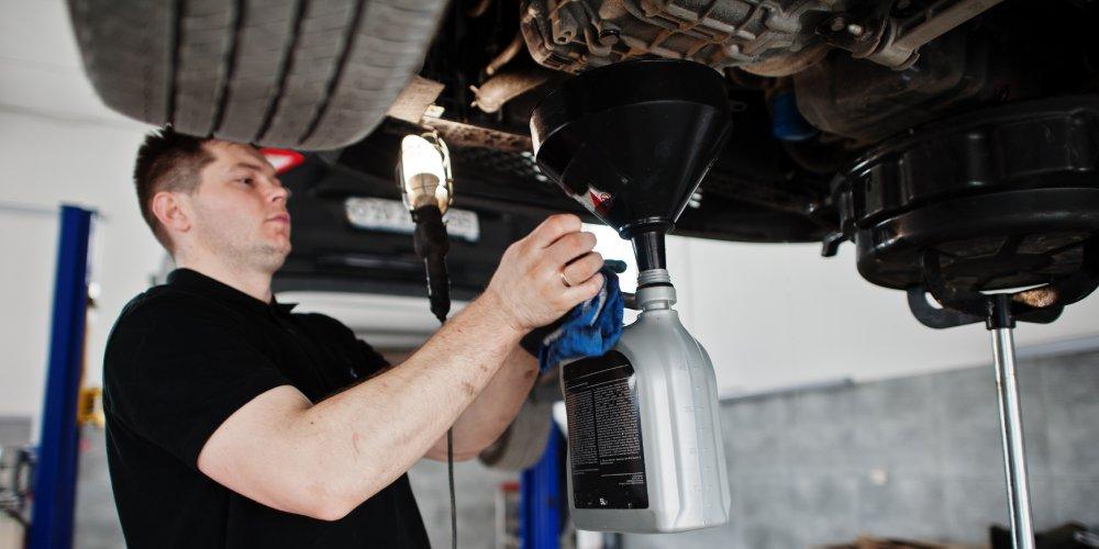 A mechanic is performing an oil change on a car elevated on a lift