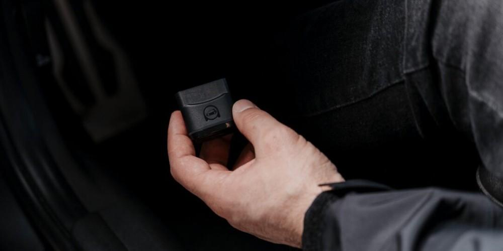 A person reaching towards the OBD2 port in a vehicle to plug in an OBDeleven diagnostic device