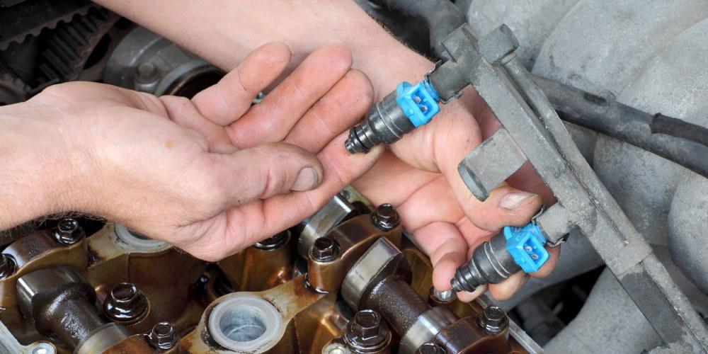 Car engine bay with a mechanic's hand holding fuel rail with fuel injectors