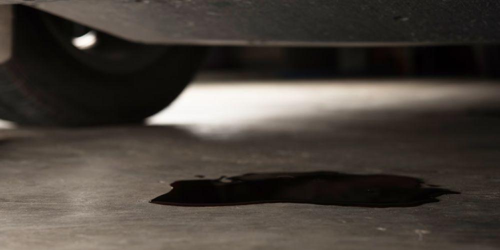  A puddle of oil on a garage floor, indicating a leak from the underside of a vehicle visible in the background.