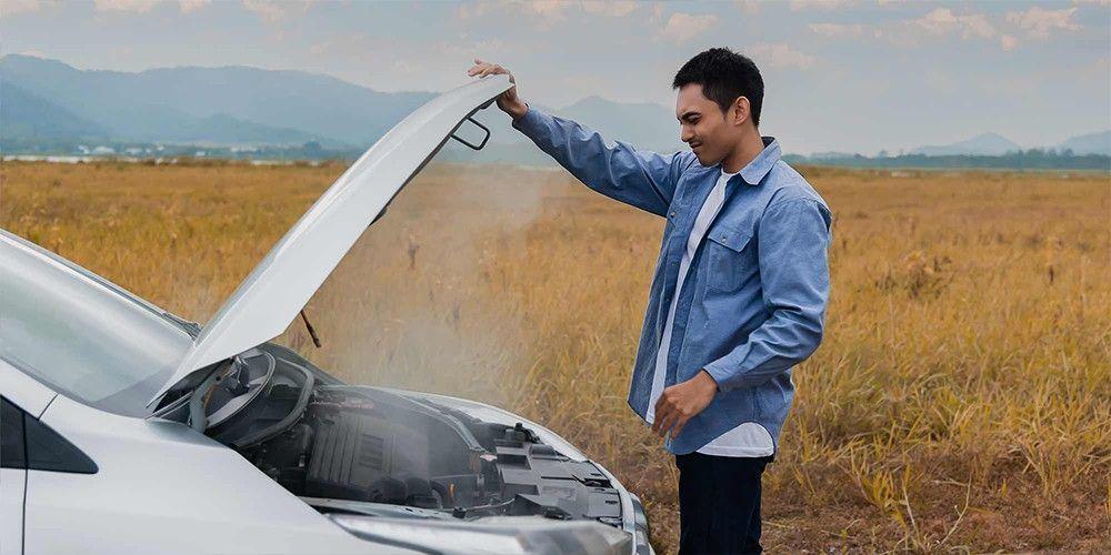 Man inspecting his car's engine with vapors rising from the open hood
