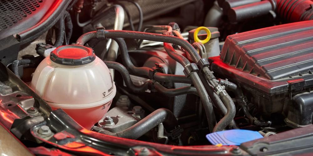  A close-up view of a car engine bay, showing a coolant reservoir, various hoses, electrical wiring, and a portion of the air intake system.